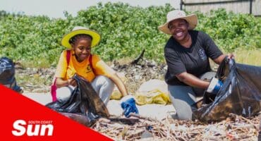 two woman sat on the beach filling refuse bags