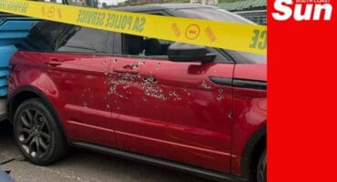 an suv behind police tape, the car has dozens of bullet holes in the driver-side door.