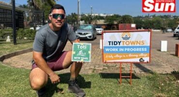 a man crouching next to a sign, holding a trail sign