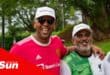 two people wearing caps and football club jerseys walk along the road