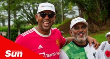 two people wearing caps and football club jerseys walk along the road