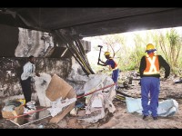 A squatter rummages through the remains of his shack while another shack is demolished by a Land Invasion worker.