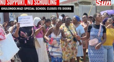 A group of women who are raising white papers with messages against the ill-treatment of the school by the Department of Education. They are also singing songs outside a locked school gate.