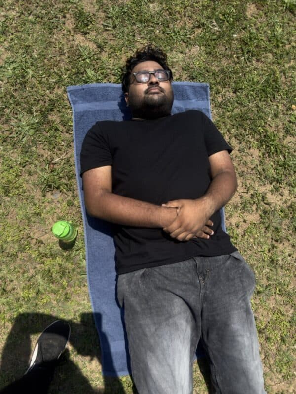 Relaxing man sunbathing on grassy area, enjoying outdoor leisure, sunny weather, summer day, Southlands Sun.