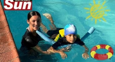 A woman helping a child float as well as kick in the swimming pool.