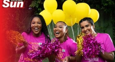 Three women wearing pink t-shirts cheering with pom poms and bright yellow balloons in the background
