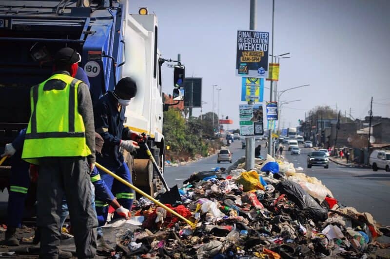 Workers of a private waste collection company clears the waste dumped on Median strip along Vincent Tshabalala Road in Alexandra on July 29, 2026.
