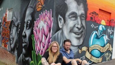 art, Street artist couple sitting in front of a mural painted on the woman's house during lockdown. The mural includes portarits of Johnny Clegg and Miriam Makeba and was done especially for the Queensburgh News to commemorate Heritage Day.
