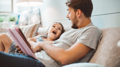 Father and daughter enjoying at home. Sitting on bed and reading book together.