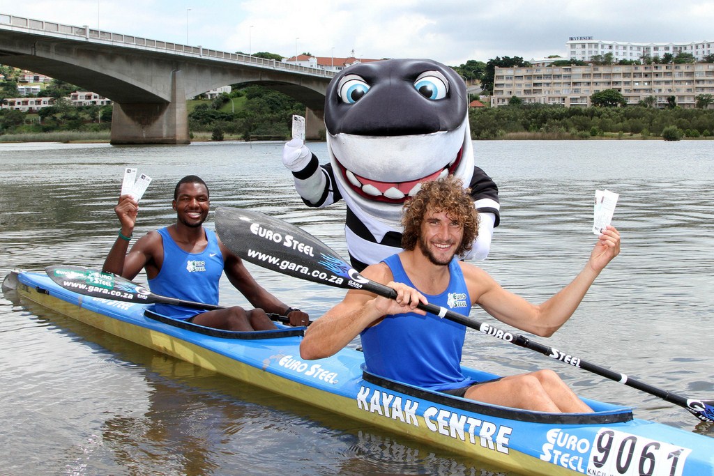 The CellC Sharks mascot Sharkie surfaces from Blue Lagoon to present pre-race favourites Sbonelo Zondi (left) and Andy Birkett with a pair of tickets to watch The Sharks take on the Bulls on the Saturday evening after final day of the race. The Sharks have given two tickets to every Dusi entrant to enjoy the game in a special Dusi block. PHOTO: Terry Haywood