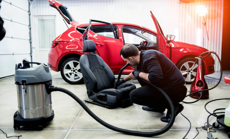 Car service worker cleaning car seat with vacuum cleaner.