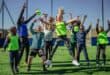 Children jump and celebrate with their coach on a sports field during an outdoor activity.