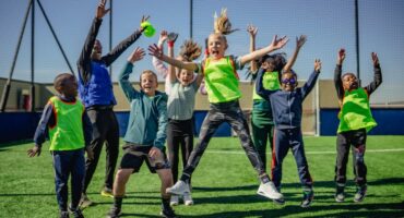 Children jump and celebrate with their coach on a sports field during an outdoor activity.