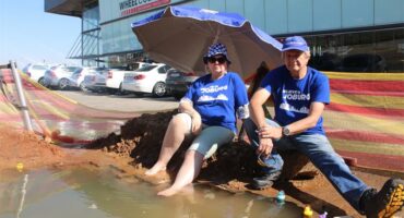 Ward 132 councillor Annette Deppe and Ward 110 PR councillor Graham de Kock sit beside a pool formed by a leaking pipe to spotlight delays in repairs on May 28. Photo: Comfort Makhanya