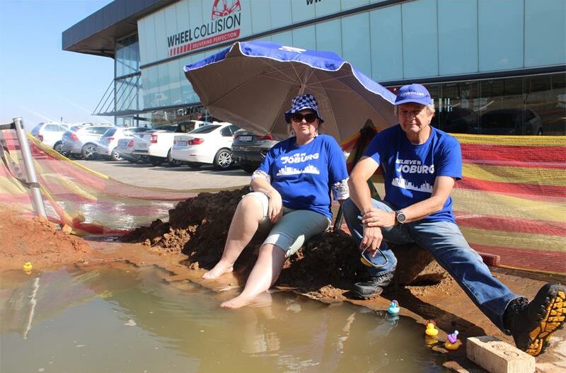 Ward 132 councillor Annette Deppe and Ward 110 PR councillor Graham de Kock sit beside a pool formed by a leaking pipe to spotlight delays in repairs on May 28. Photo: Comfort Makhanya