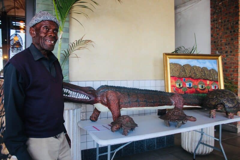 Artist Richard Ngojo stands next to his artworks, titled The Predator, Impiloende, and Village (Home sweet home) at the auction on August 2, 2026. Photo: Zanele Mfaba