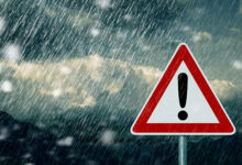 An image of bad weather conditions - dark clouds and lightning seen in the image with a warning sign in front of the image.