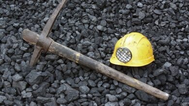 A yellow hat and a pick lying on coal at a coal mine.