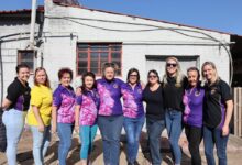 A group of woman dressed in purple pose for a photo. All of them are posed in front of an old, white building.