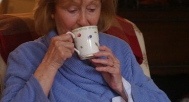Woman wearing warm gown and drinking tea in her lounge.