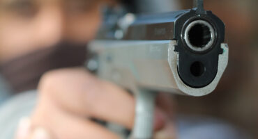A photo of a man with his face blurred holding a gun.