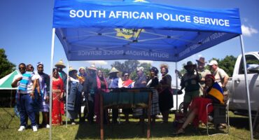 Amajuba District SAPS members dressed in traditional attire stand under a South African Police Service tent during Heritage Day celebrations.