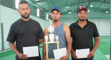Three indian males are pictured standing infront of a net. All three men are holding envelopes while the middle man is holding a trophy. The image is pictured during an angling prize giving ceremony.