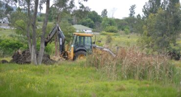 Image of a yellow plant machine in a field with workers to carry out water line repairs.