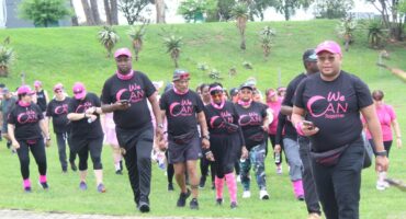 A diverse group of people dressed in black and pink attire, walking outdoors together forcancer awareness at Greygoose Game Lodge in Newcastle.
