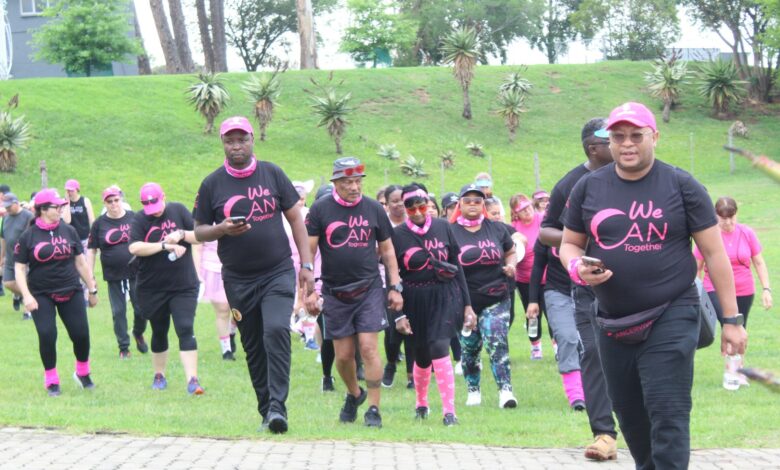 A diverse group of people dressed in black and pink attire, walking outdoors together forcancer awareness at Greygoose Game Lodge in Newcastle.