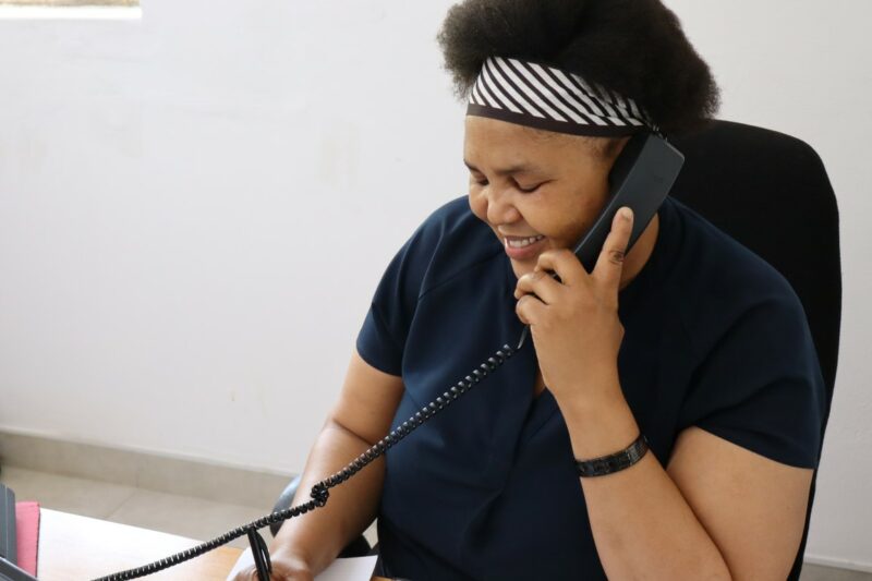 Philile is talking on the telephone with a client while writing the information down