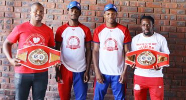 Photo of Dundee boxers and coach with belt in front of wall.