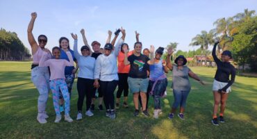 Group of women, black and white, dressed in active gear throwing their arms in the air at parkrun event.