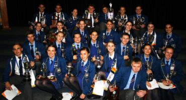 Hoërskool Pionier learners dressed in blue uniform sitting on steps holding their trophies.