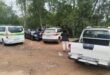 Several police officers stand near marked police vehicles in a wooded area at the Newcastle bus rank, engaging in conversation while at a scene of a deceased person found floating in the river.