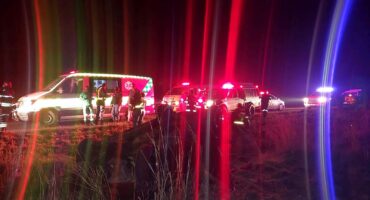 Various emergency vehicles with blue and red lights attend to an overturned vehicle alongside a rural road near Utrecht.