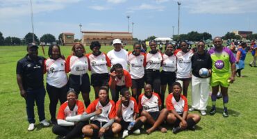 The Newcastle Boschpick Highlanders women's rugby team poses on a sunny field, wearing red and white uniforms.
