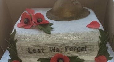 A square cake, covered in silver icing with red poppy flowers on it and a 'tin hat' representing the MOTHS.