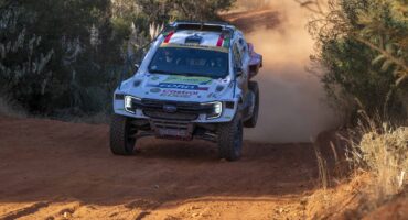 White Ford race car speeding on gravel road with dust behind it.