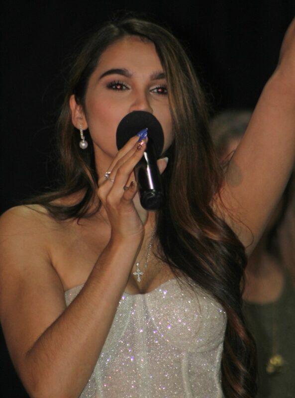 A beautiful young lady dressed in an evening gown talking over a microphone.