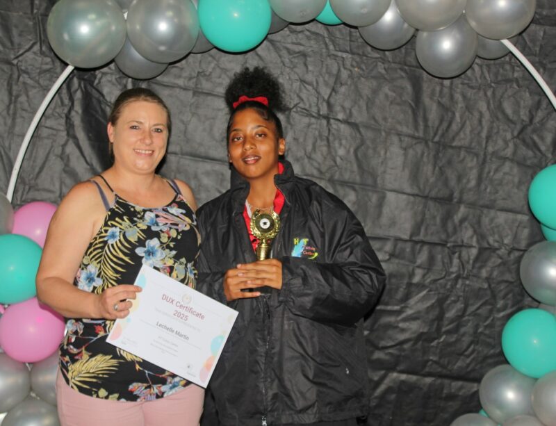 Two girls pose in front of a black and coloured baloon background holding certificates during a prize giving ceremony.