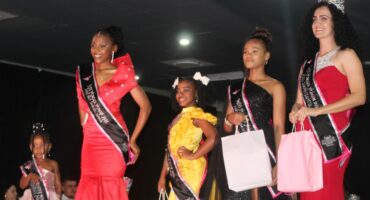 Five beauty queens standing with their sasses, crowns and prizes on a stage after the Miss Wonder Woman Pageant in Newcastle.