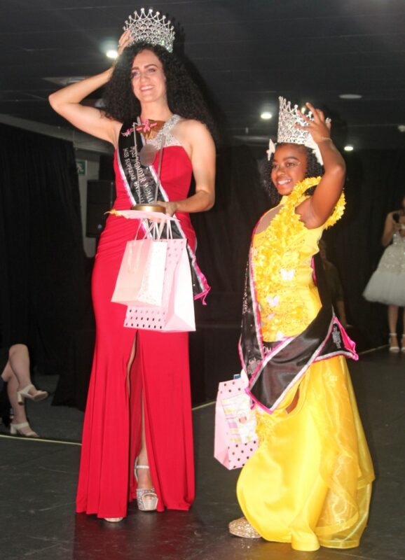 Two beauty queens dressed in beautiful evening wear, wearing sashes and crowns on the Miss Wonder Woman Beauty Pageant Stage.