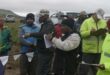 A group of fishermen dressed in the fisherman attire standing outside by a large Chelmsford Dam.