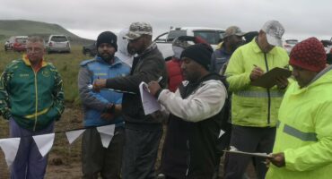 A group of fishermen dressed in the fisherman attire standing outside by a large Chelmsford Dam.