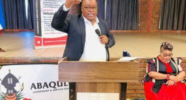 An Image of AbaQulusi Local Municipality Mayor, Sifiso Mkhwanazi standing at a podium, holding a micro-phone addressing ward committees at Cecil Emmett Hall.