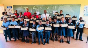 A group image of Nkwambazi Primary School learners and staff members. Each learner is holding a box with school shoes donated by an NPO.