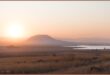 A photograph capturing the sunset over the Ntshingwayo (chelmsford) Dam. Also in the photo is a reddish/ pink sky, a little mountain, grasslands and the dam.