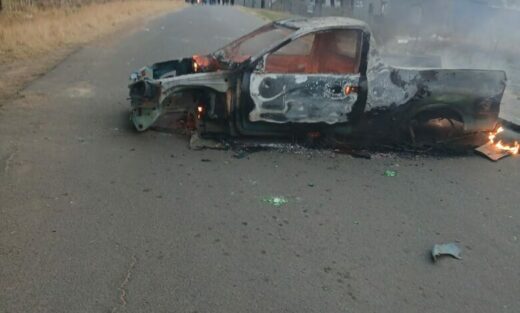 Image of a burnt out bakkie standing in the middle of the road.