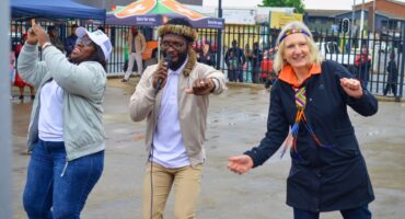 A black woman and man dancing with a white woman dressed in black and Zulu attire.